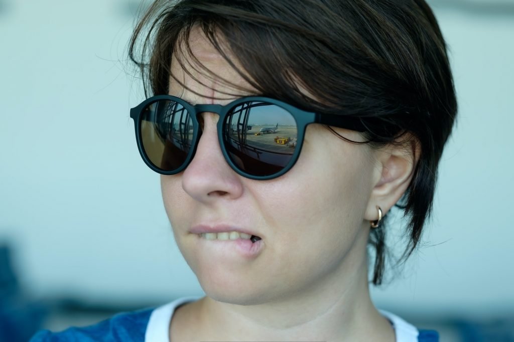 A woman is afraid to fly. She looks at the plane with fear. Focus on sunglasses reflection
