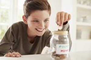 Boy Saving Pocket Money In Glass Jar At Home