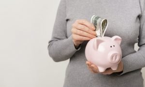 Unrecognizable woman putting cash into piggy bank