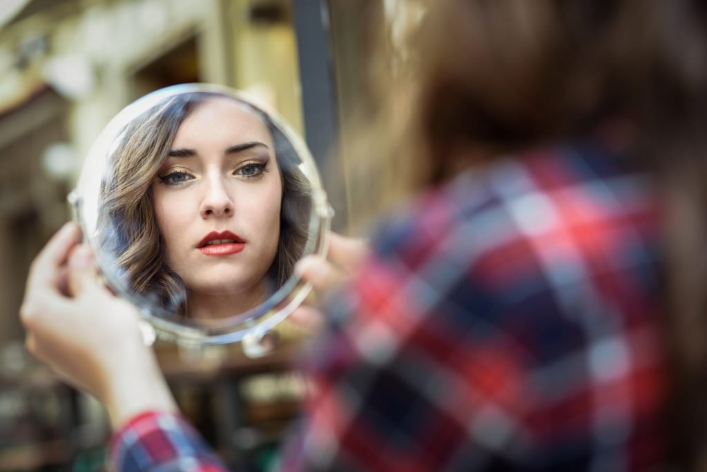 Young woman looking at herself in a little mirror