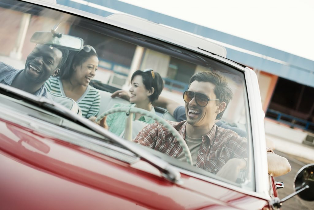 A group of friends in a red convertible car on a road trip.