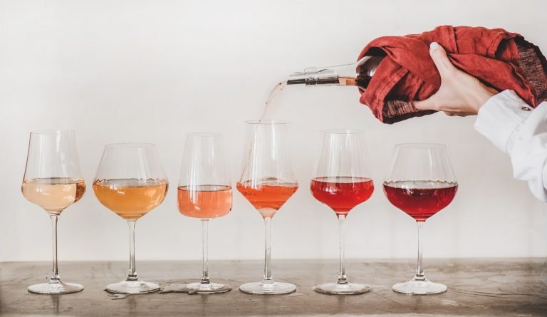 Rose wine glasses and womans hand pouring wine, white background