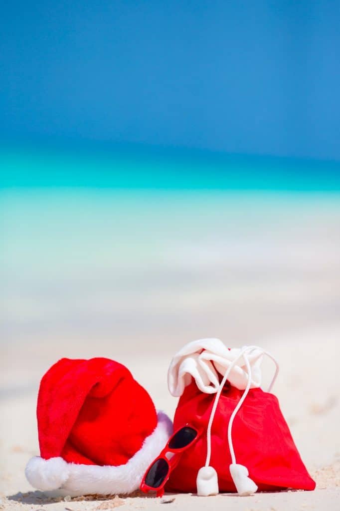 Closeup of red Santa bag and Santa Claus hat on beach. Xmas travel vacation and travel cuprise