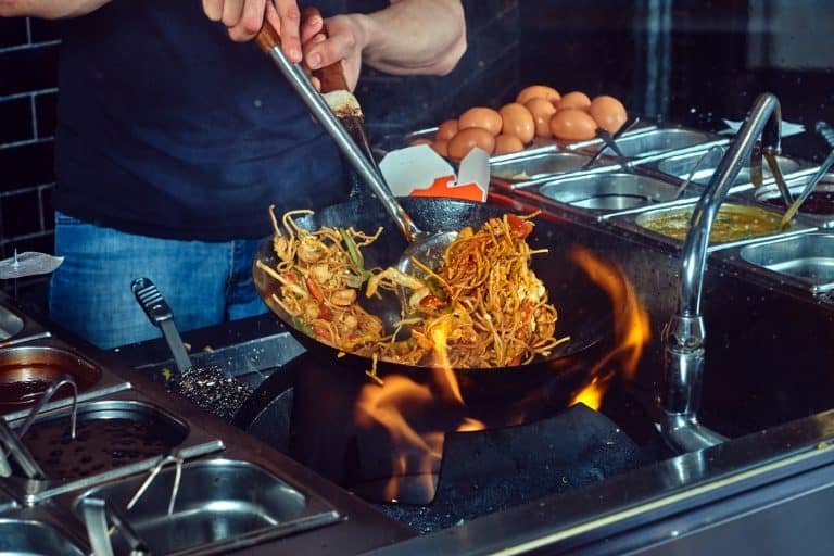 Cooking process in an Asian restaurant. Cook is fry vegetables with spices and sauce in a wok