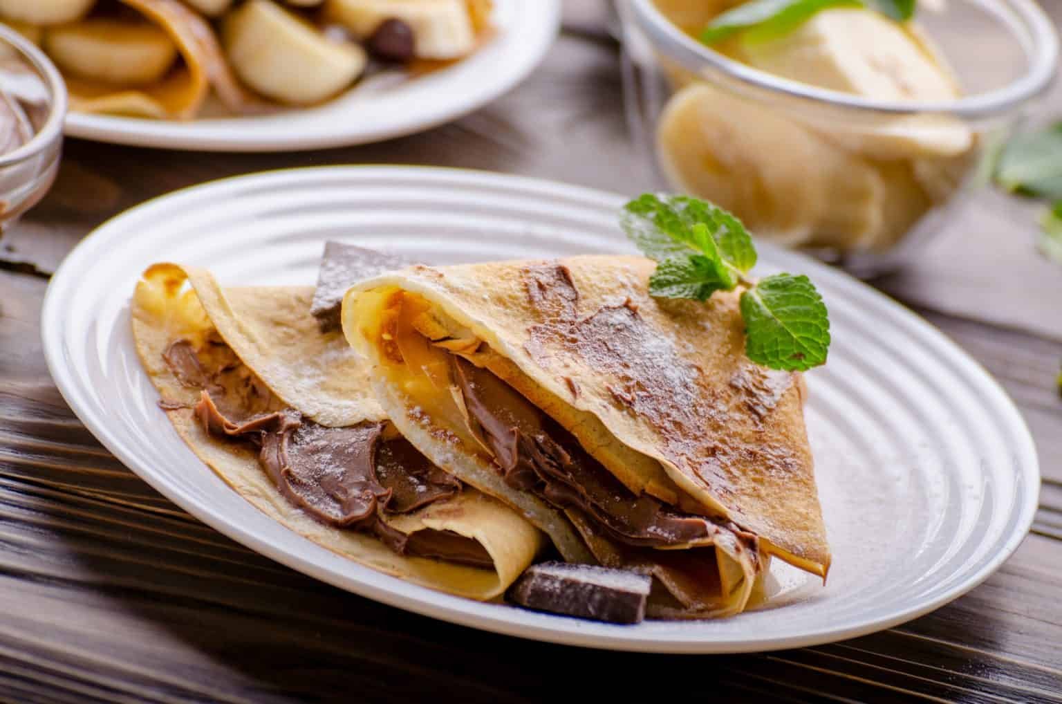 French crepes with chocolate sauce and banana in ceramic dish on