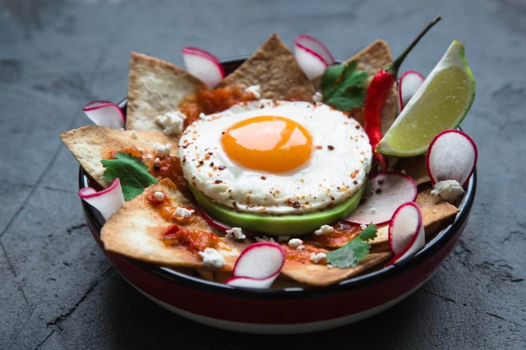 Mexican breakfast: chilaquiles with egg, avocado and vegetables close-up on a plate