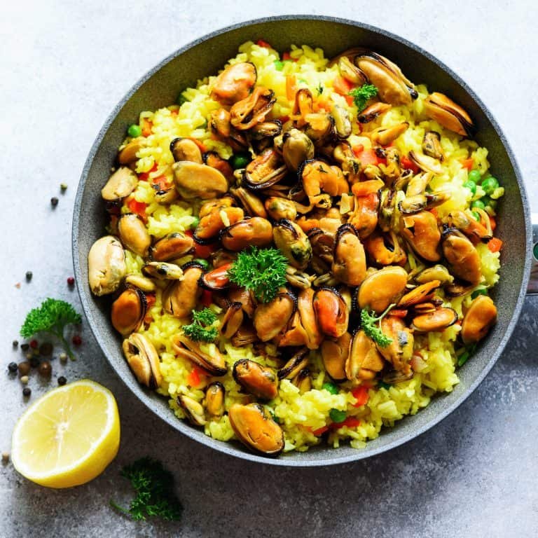 Traditional spanish seafood paella in pan rice, peas, shrimps, mussels, squid on light grey concrete