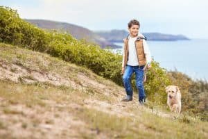 Boy Exercising Dog On Leash Walking Up Hill By Sea