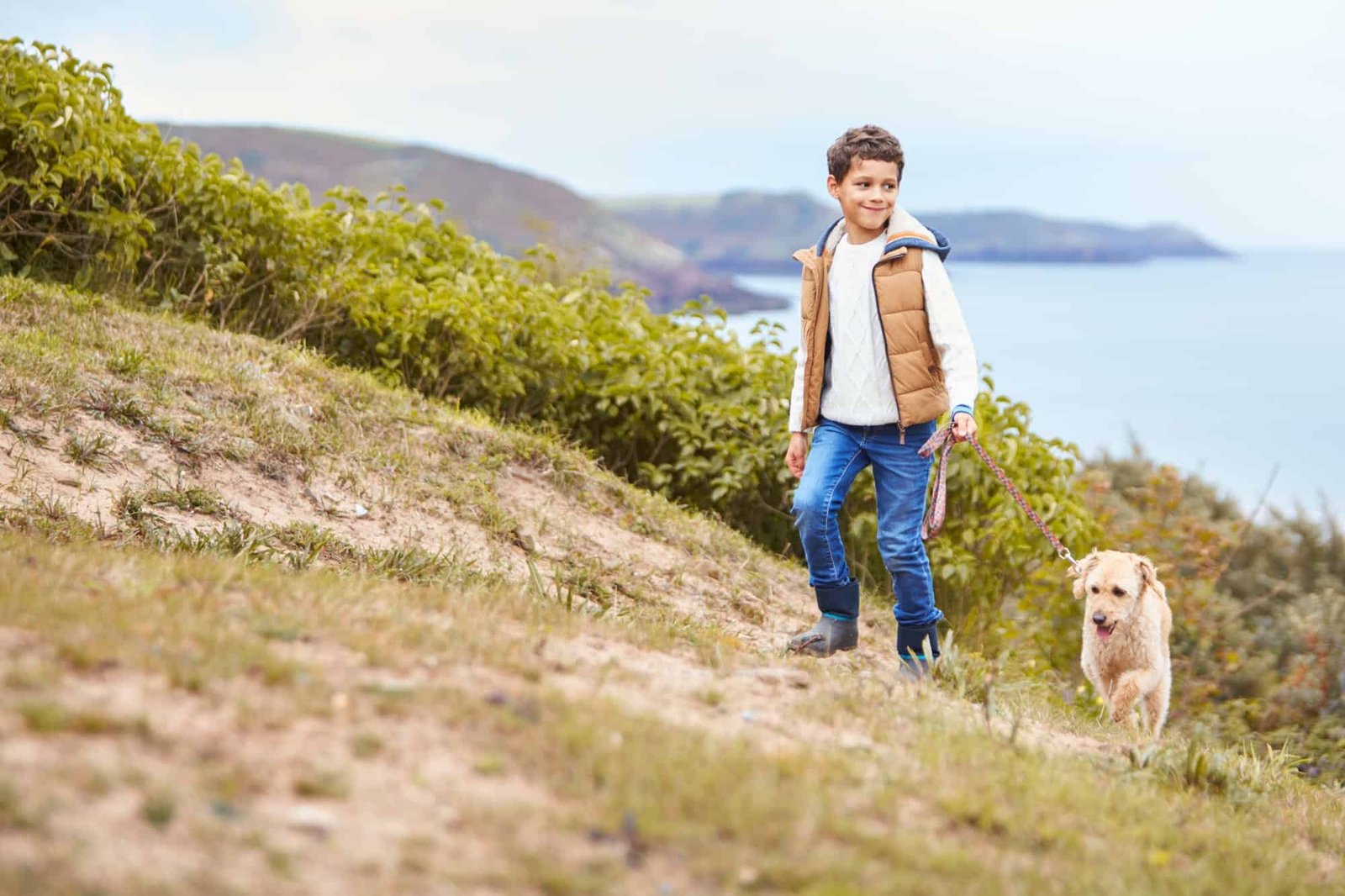 Boy Exercising Dog On Leash Walking Up Hill By Sea