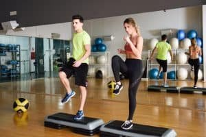 Two people working out with steppers in gym.