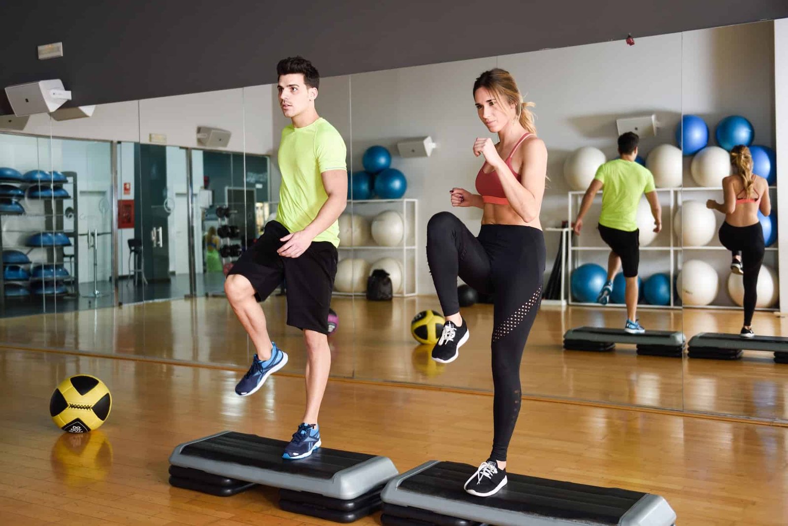 Two people working out with steppers in gym.
