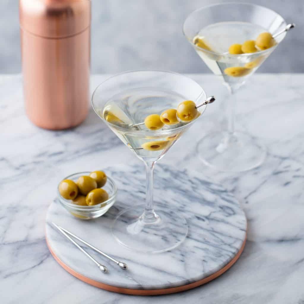 Martini Cocktail with Olives and Bar Shaker on Marble Table Background.
