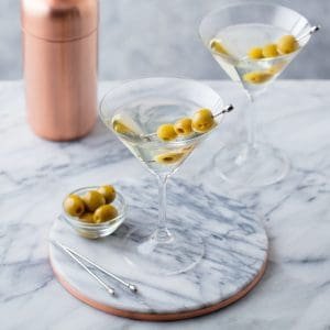Martini Cocktail with Olives and Bar Shaker on Marble Table Background.