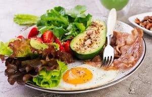 Plate with a keto diet food. Fried egg, bacon, avocado, arugula and strawberries. Keto breakfast.