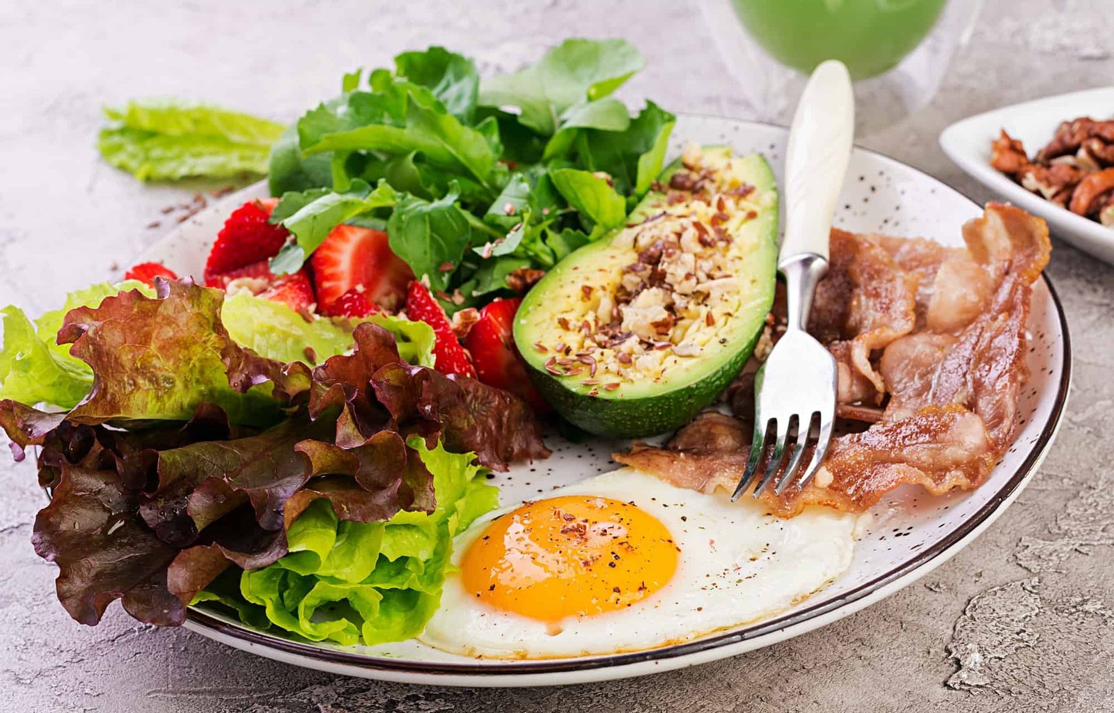 Plate with a keto diet food. Fried egg, bacon, avocado, arugula and strawberries. Keto breakfast.