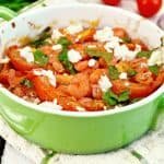 Shrimp and tomato with feta in green pan on light board