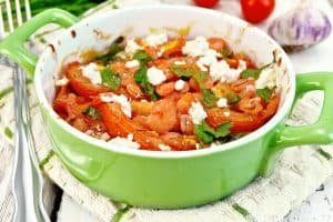Shrimp and tomato with feta in green pan on light board