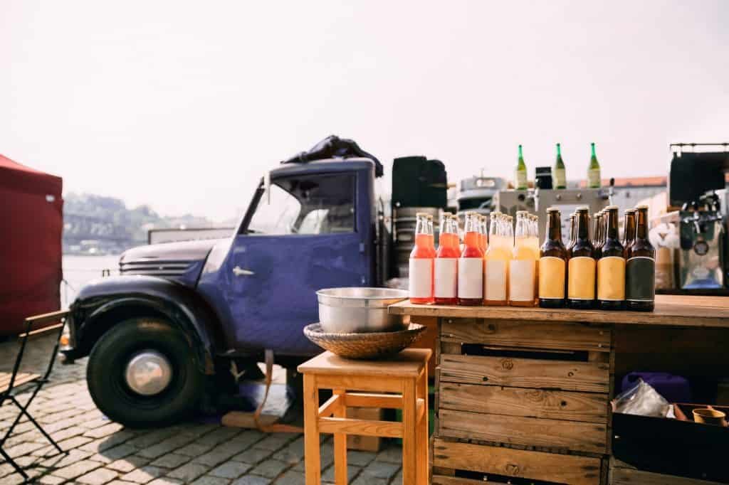 Lemonade, Cider And Other Drinks In Bottles Are Exhibited On A Wooden Counter Near Truck With Food